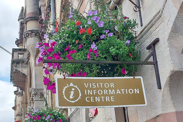 A visitor information centre sign under a hanging basket of flowers